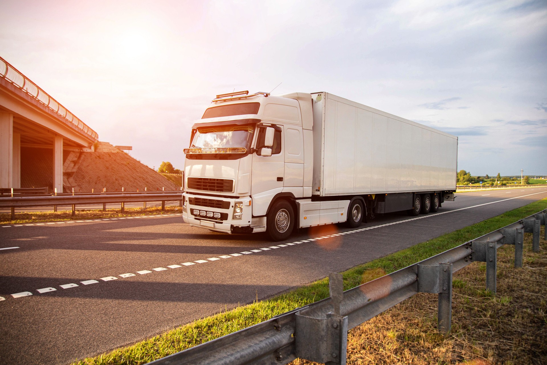 A white modern truck with an isothermal refrigerated semi-trailer transports perishable products in a trailer with a constant temperature regime. Transportation of seafood, fruits and meat. Copy space for text, sunset