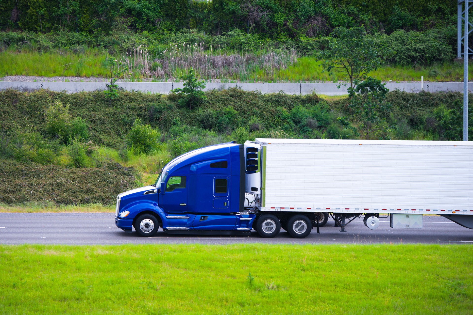 Modern dark blue semi truck reefer trailer profile on road